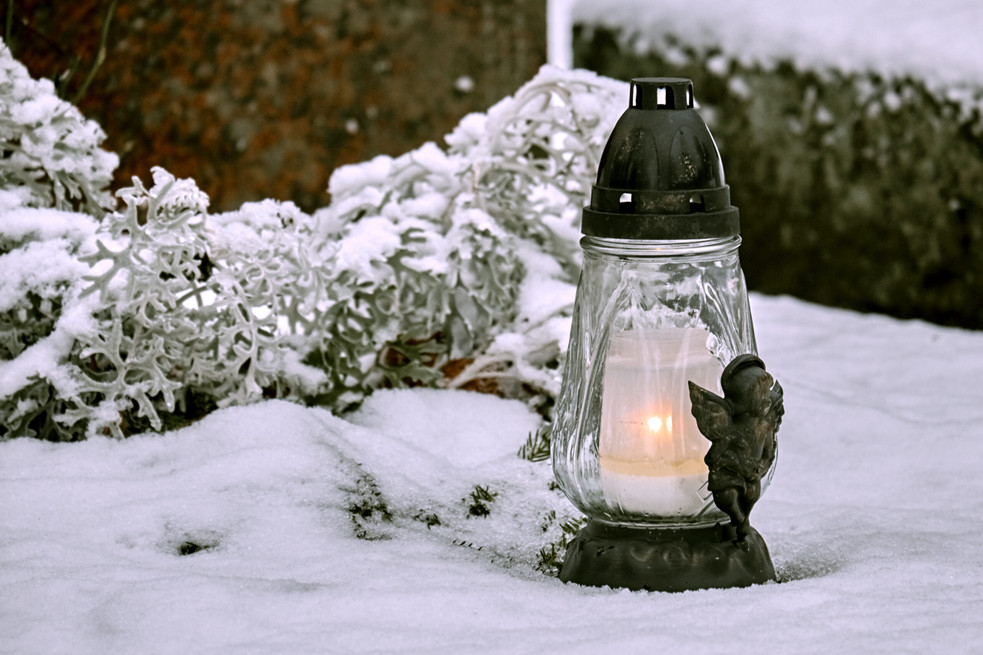 Lantern with candle at the grave covered with snow in winter.