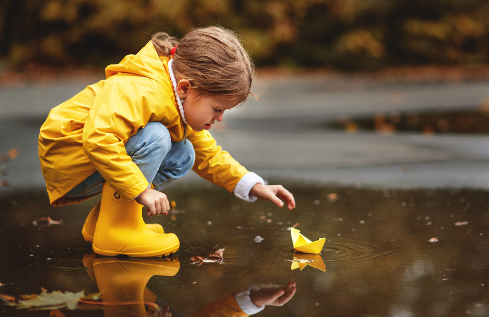 happy child girl with umbrella and paper boat in a puddle in   autumn on nature