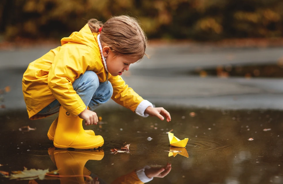 happy child girl with umbrella and paper boat in a puddle in   autumn on nature